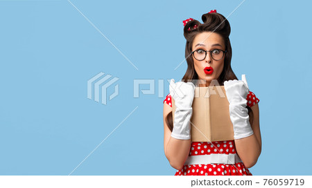 Shocked pinup woman reading book with eyes wide open on blue studio background, banner design with copy space 76059719