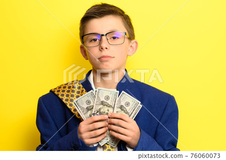 A boy in glasses and an oversized suit with a satisfied face is holding US dollars, a child and big money. A boy in glasses and an oversized suit with a satisfied face is holding US dollars, a child and big money. 76060073
