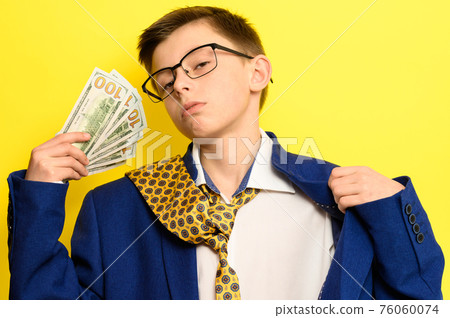 A guy in a big classic suit on a yellow background holds a foreign currency, a child in glasses and a suit with a tie. A guy in a big classic suit on a yellow background holds a foreign currency, a child in glasses and a suit with a tie. 76060074
