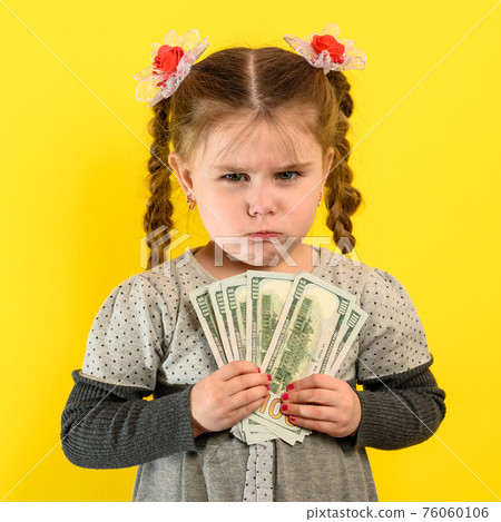 Portrait of a girl on a yellow background, a child holding money in his hands, a large amount of money, a US dollar and a child. Portrait of a girl on a yellow background, a child holding money in his hands, a large amount of money, a US dollar and a child. 76060106