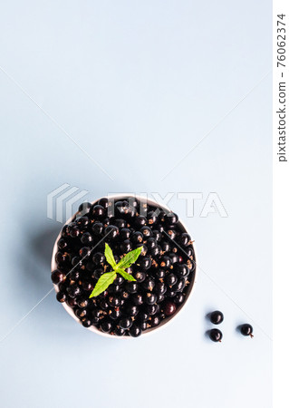 Organic blackcurrant berries in white glass cup and scattered around isolated on blue background. Top view. Flat lay Summer harvest concept Organic blackcurrant berries in white glass cup and scattered around isolated on blue background. Top view. Flat lay Summer harvest concept 76062374