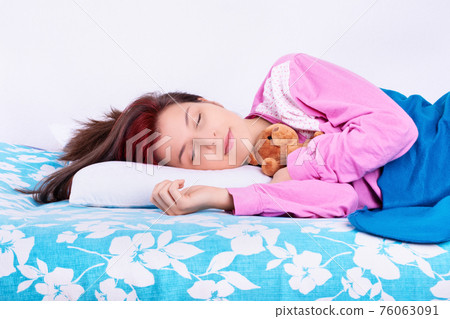 Young woman sleeping calmly in her bed hugging teddy bear 76063091