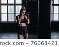 Athletic fit female boxer exercising punches with boxing bag in gym during kickboxing and self defense intensive workout 76063421