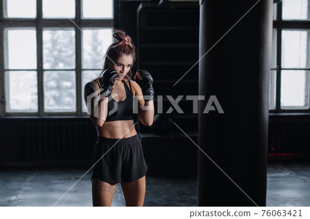 Athletic fit female boxer exercising punches with boxing bag in gym during kickboxing and self defense intensive workout 76063421