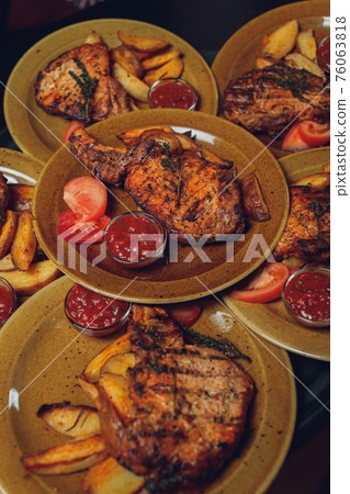 Cast iron plate with sliced grilled rib-eye steak on table with yellow potato wedges and oil in saucer over table with copy space. 76063818
