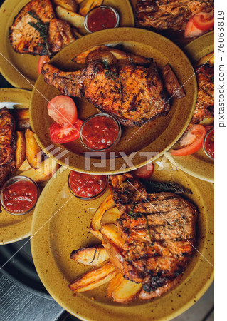 Cast iron plate with sliced grilled rib-eye steak on table with yellow potato wedges and oil in saucer over table with copy space. 76063819