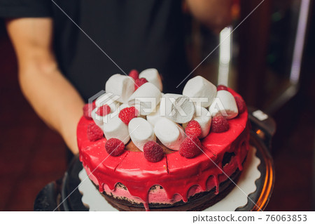 Happy Canada Day celebration cake with flags, marshmallow and candy decorations on a red cake stand on a white table against a red background. 76063853