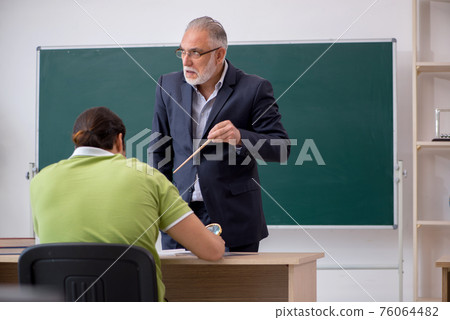 Aged teacher and young male student in the classroom Aged teacher and young male student in the classroom 76064482
