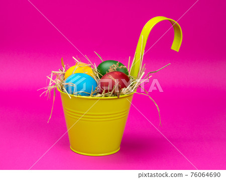 Easter eggs on the hay in a bright bucket. Pink background. Easter eggs on the hay in a bright bucket. Pink background. 76064690