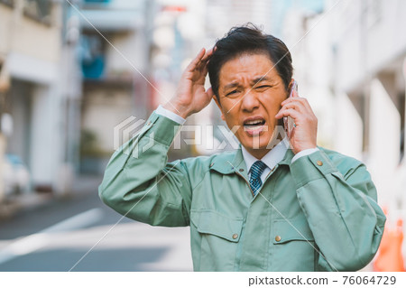 A man in work clothes and a tie gets angry on the phone A man in work clothes and a tie gets angry on the phone 76064729