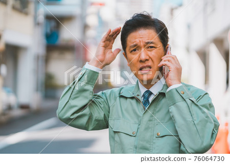 A man in work clothes and a tie gets angry on the phone A man in work clothes and a tie gets angry on the phone 76064730