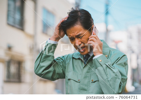 A man in work clothes and a tie gets angry on the phone A man in work clothes and a tie gets angry on the phone 76064731
