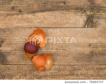 A painted egg and onion husk on a wooden background. 76064747