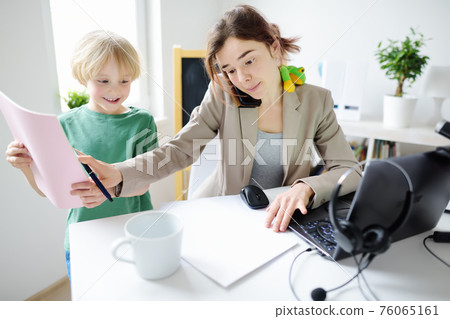 Young woman working from home with laptop during quarantine. Home office and parenthood at same time. Exhausted parent with hyperactive child. 76065161