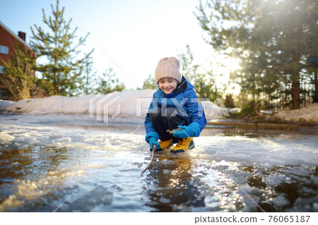 Cute preschooler boy is playing with a stick in brook on sunny day. Child having fun and enjoy a big puddle. All kids love play with water. Happy childhood. Outdoor activity for baby in sping Cute preschooler boy is playing with a stick in brook on sunny day. Child having fun and enjoy a big puddle. All kids love play with water. Happy childhood. Outdoor activity for baby in sping 76065187