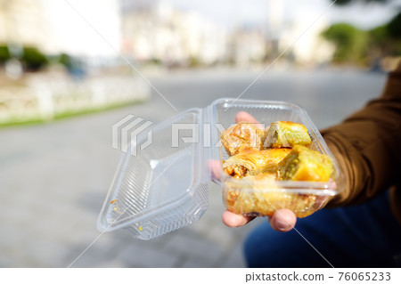 A male tourist bought a baklava and is going to try it. Traditional turkish dessert Baklava. Ramadan dessert. A male tourist bought a baklava and is going to try it. Traditional turkish dessert Baklava. Ramadan dessert. 76065233