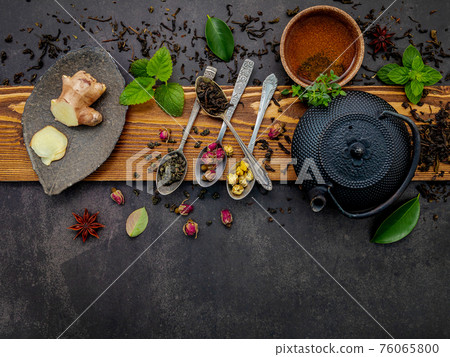 Black cast iron tea pot with herbal tea set up on dark stone background. 76065800