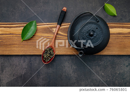 Black cast iron tea pot with herbal tea set up on dark stone background. 76065801