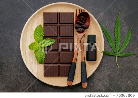 Food conceptual image of cannabis leaf with dark chocolate and fork on dark concrete background. Food conceptual image of cannabis leaf with dark chocolate and fork on dark concrete background. 76065809
