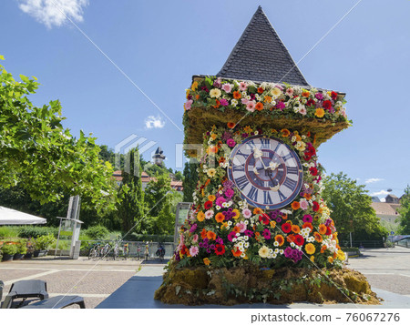 The famous clock tower, one of the city of Graz attractions, made of flowers and the real Clock Tower (Grazer Uhrturm) in the background in Styria region, Austria, in sunny spring day 76067276