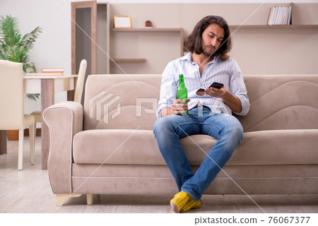 Young man drinking alcohol at home 76067377