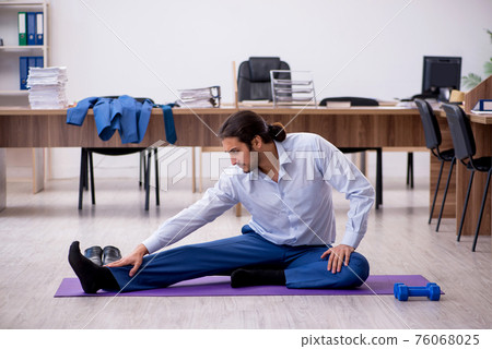 Young male employee doing sport exercises during break 76068025