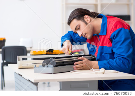 Young repairman repairing air-conditioner at warranty center Young repairman repairing air-conditioner at warranty center 76070053