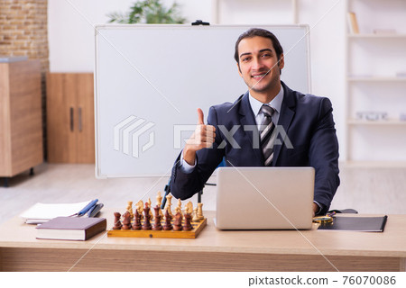 Young male employee playing chess at workplace 76070086