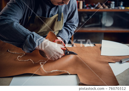 A talented young guy helps his father in the family business, cuts out blanks for shoes from leather 76070312