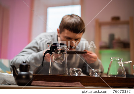 A man in an intimate home environment prepares for a Chinese tea ceremony, inhales the aroma of fresh raw black tea. A man in an intimate home environment prepares for a Chinese tea ceremony, inhales the aroma of fresh raw black tea. 76070382