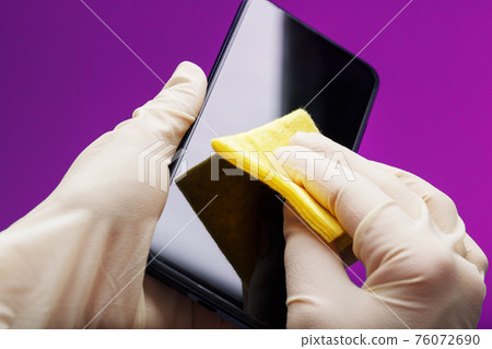 Preventive cleaning of a smartphone with a yellow napkin from dirt in rubber gloves on a pink background. 76072690