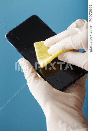 Hands in protective gloves clean and disinfect a smartphone with a yellow napkin on a blue background. 76072691