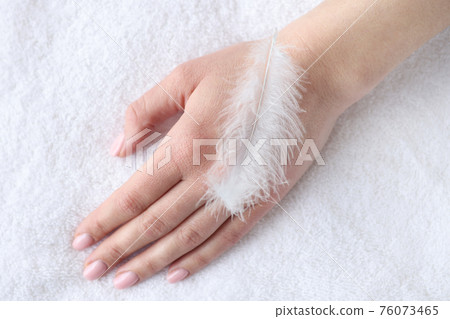 Soft white feather lying on woman hand closeup 76073465