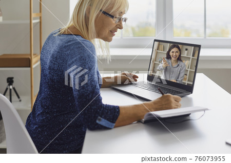 Mature lady taking notes while watching online lecture or having video call with coach 76073955