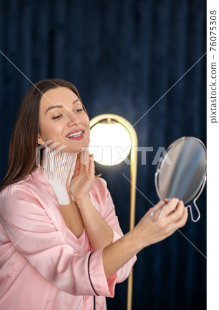 Young woman in pink lingerie and with tapes on her neck looking in the mirror and smiling 76075308