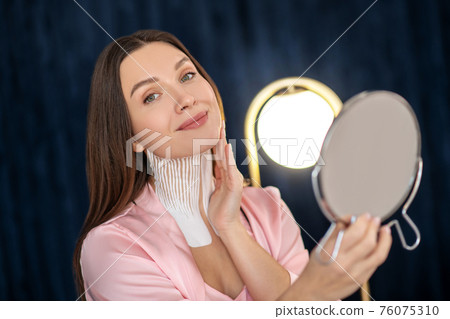 Young woman in pink lingerie and with tapes on her neck looking in the mirror and smiling 76075310