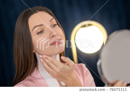 Young woman in pink lingerie and with tapes on her neck looking in the mirror 76075311