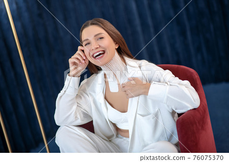 Young woman with tapes on her neck sitting on a chair and looking cheerful 76075370