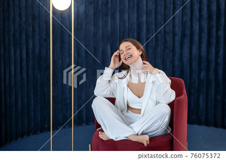 Young woman with tapes on her neck sitting on a chair and looking cheerful 76075372