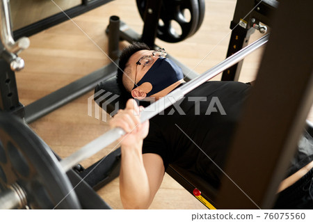Asian man wearing a mask and doing a bench press Asian man wearing a mask and doing a bench press 76075560