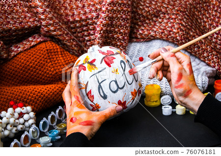 DIY. Do it yourself. Woman paints thanksgiving decorations on orange pumpkin for Halloween. Autumn harvest. 76076181