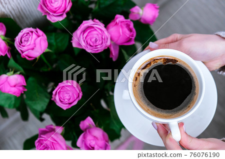 Cup of coffee and pink roses. Holiday concept, bouquet of roses for a birthday, bouquet of flowers in the morning breakfast. Female hands holding cappuccino Cup of coffee and pink roses. Holiday concept, bouquet of roses for a birthday, bouquet of flowers in the morning breakfast. Female hands holding cappuccino 76076190