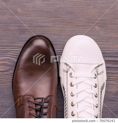 Men's classic brown shoes and white sneakers on a wooden background. Top view Men's classic brown shoes and white sneakers on a wooden background. Top view 76076241