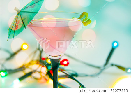 pink cosmopolitan drink with lemon peel and string lights 76077313