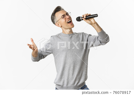 Portrait of passionate middle-aged man singing serenade in microphone, standing carefree over white background Portrait of passionate middle-aged man singing serenade in microphone, standing carefree over white background 76078917