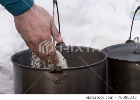 Close-up of a man's hand, which pours products into the pot. Cooking pot for cooking over a fire. Tourism Close-up of a man's hand, which pours products into the pot. Cooking pot for cooking over a fire. Tourism 76080338