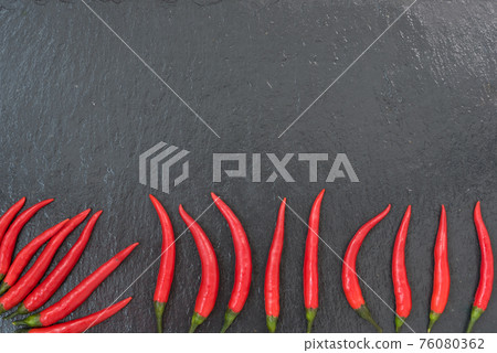 Red chili peppers are laid out on a black slate background. There is room for text Red chili peppers are laid out on a black slate background. There is room for text 76080362