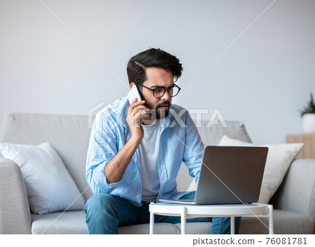 Busy Eastern Freelancer Guy Talking On Phone And Using Laptop At Home Busy Eastern Freelancer Guy Talking On Phone And Using Laptop At Home 76081781