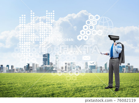 Camera headed man standing on green grass against modern cityscape Camera headed man standing on green grass against modern cityscape 76082119