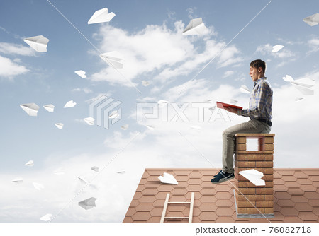 Handsome student guy reading book and paper planes flying in air Handsome student guy reading book and paper planes flying in air 76082718